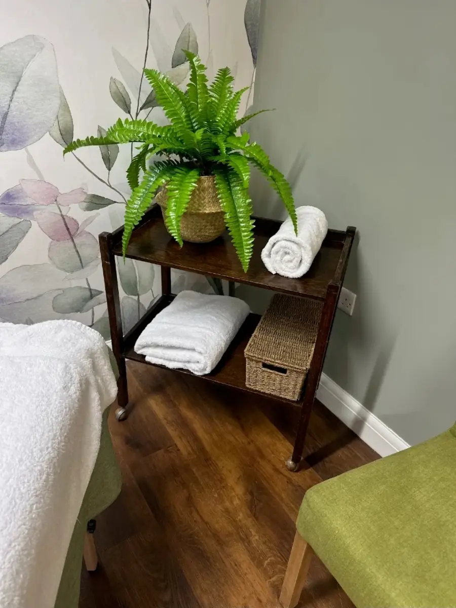 A wooden trolley with a fern in a woven basket and rolled white towels